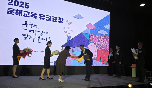 2025 문해교육 유공표창 시상식 현장. 수상자가 무대 위에서 관계자에게 상장을 전달받고 있으며, 배경 스크린에는 “2025 문해교육 유공표창, 문해, 세상이 달라보이죠”라는 문구와 함께 교육부 및 관련 기관 로고가 표시되어 있다.